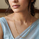 A close-up of a woman wearing a delicate gold chain necklace with a figure-eight pattern, styled with a light blue draped top.